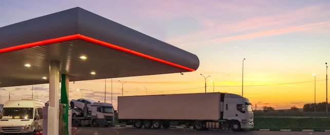 Stacja benzynowa, na której stoi ciężarówka, na tle wschodzącego słońca.